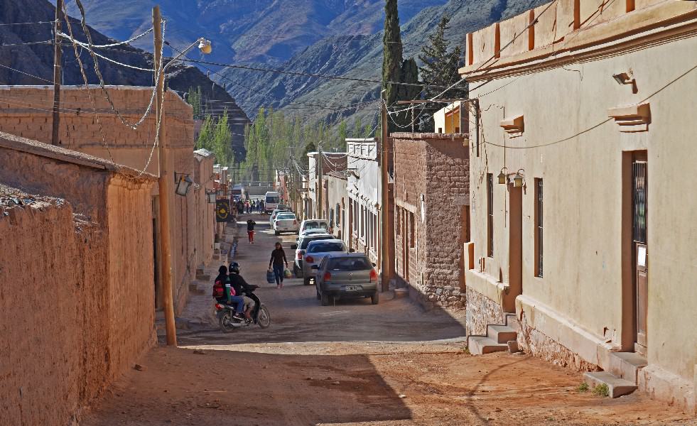 This snapshot captures the essence of Purmamarca's streets. A quaint and narrow thoroughfare winds through the charming town, lined with simple buildings adorned in vibrant colors. The street is bustling with life, as a few cars navigate their way through the picturesque surroundings. The scene is a blend of simplicity and authenticity, showcasing the unique character of this Andean village. As you explore the streets of Purmamarca, you'll be immersed in its rich cultural heritage and enchanting atmosphere.