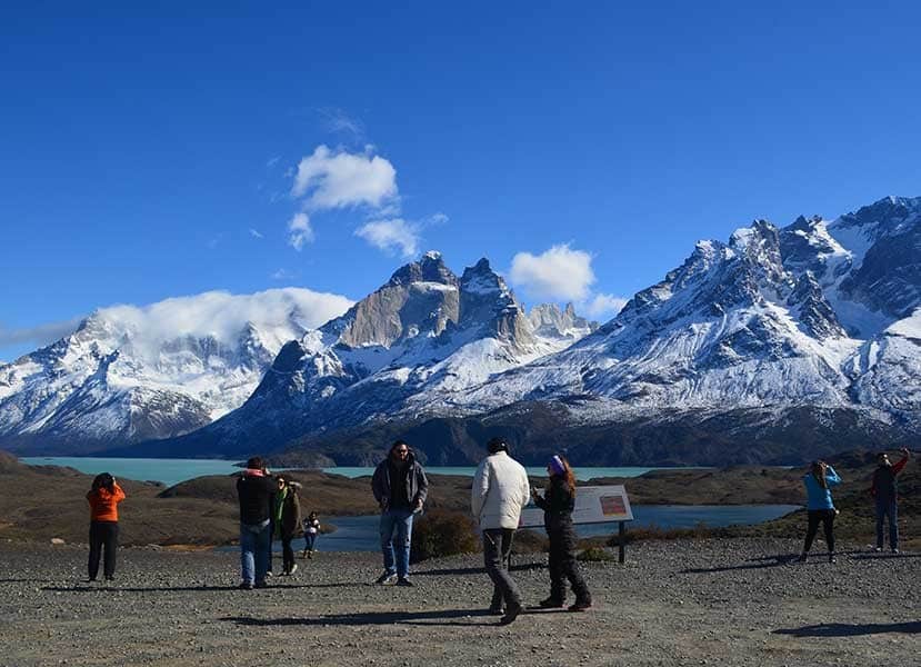 amazing Image with blue sky, a snowcapped mountain range and a milky blue lagoon infront of the mountain range. Tourists gathered infront and taking pictures of the mountains and the few clouds covering the peaks.