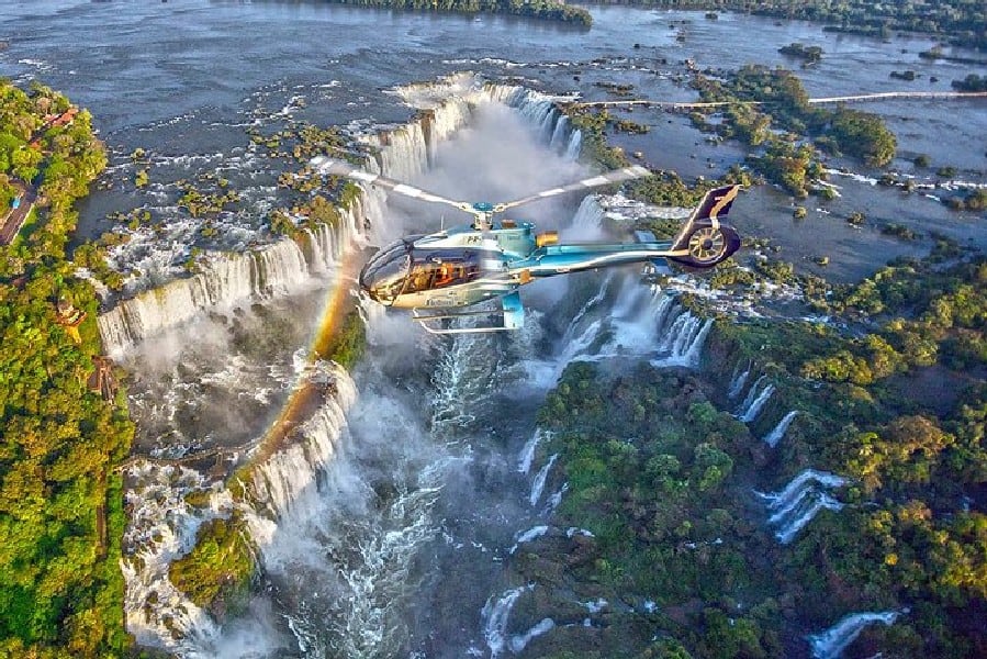 This breathtaking picture captures the awe-inspiring Iguazu Falls from a helicopter tour. From this aerial perspective, the majestic waterfalls come into full view, showcasing the sheer power and beauty of nature. The falls, located on the border of Argentina's Misiones province and Brazil's Paraná state, form the largest waterfall system in the world. The Iguazu River cascades down, dividing into the upper and lower sections, offering a mesmerizing spectacle. As the falls roar, the legend of Naipí and Tarobá, immortalized in Guarani folklore, echoes through the misty air. It was Spanish Conquistador Álvar Núñez Cabeza de Vaca who first documented the existence of these magnificent falls in 1541.