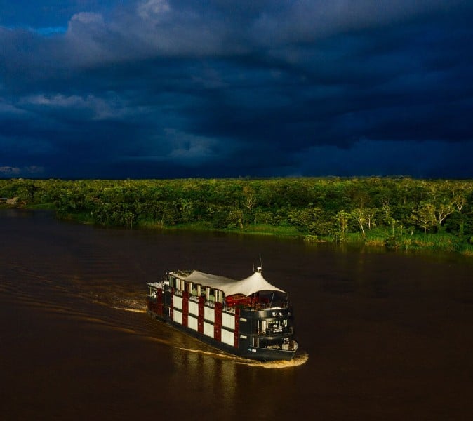 The Aria Amazon cruise on the Amazon river with the lushes green jungle and the dark clouded sky in the background.