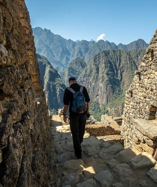 walking down Incan made stairs in Machu Picchu with the scenic mountain range in the back and a clear blue sky.