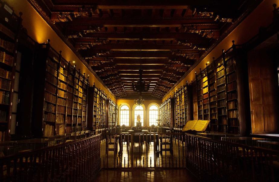 Step into the remarkable Santo Domingo Library in Lima, a sanctuary of knowledge and tranquility. Browse the extensive bookshelves and marvel at the carefully curated furniture that fills the room. Sunlight gracefully streams through multiple-paned windows, casting a warm glow. A captivating statue stands near one of the windows, enhancing the ambiance. Admire the ornate gate at the back of the room, accessible via a railing in the foreground. The lofty ceiling boasts intricate designs, adding to the library's grandeur. Relax on scattered chairs, inviting visitors to immerse themselves in the world of literature. Experience a haven of wisdom and solace within the inviting walls of this remarkable library.