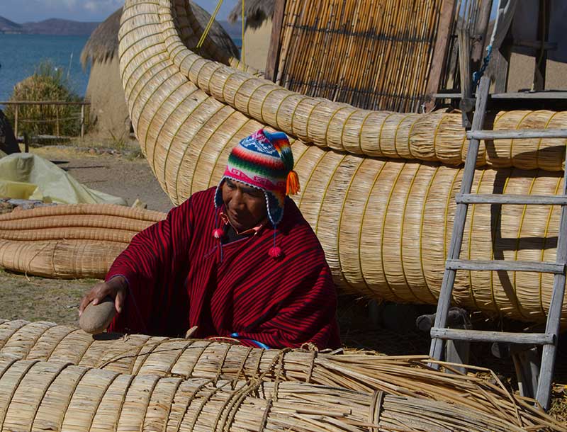 Man wearing a red poncho and a typical Andean hat is building a reed boat on Lake Titicaca 
