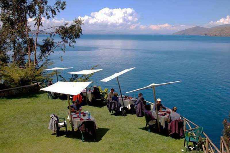 Tourists sitting on tables on a garden overlooking Titicaca Lake  