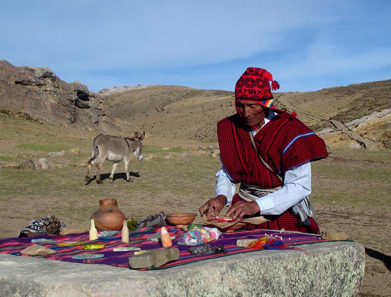 Kallawaya healer (a man wearing a red poncho and traditional Andean hat) preparing a blessing ceremony open air