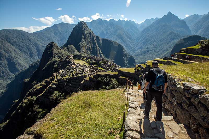 Tourists going along a path within Machu Picchu facing the Huchuy Picchu Mountain and Wayna Picchu