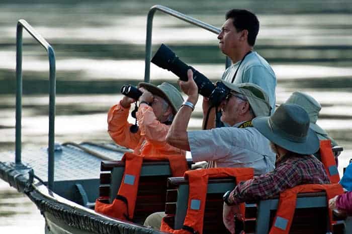 A guide with tourists during a boat excursion spotting wildlife with binoculars and a large camera lens in the Peruvian Amazon