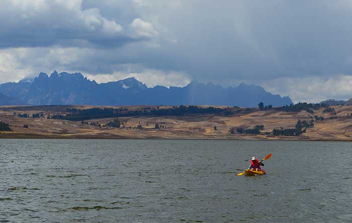 Traveler doing kayaking at the Huaypo Lake in the Sacred Valley of the Incas in Cusco with the Andean mountains as backdrop