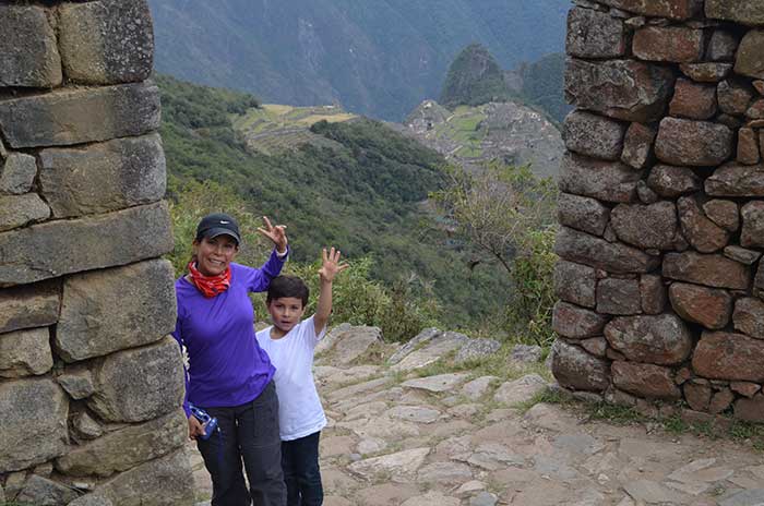 Machu Picchu With Kids A traveler with kid waving with Machu Picchu as background at Inti Punku Sun Gate