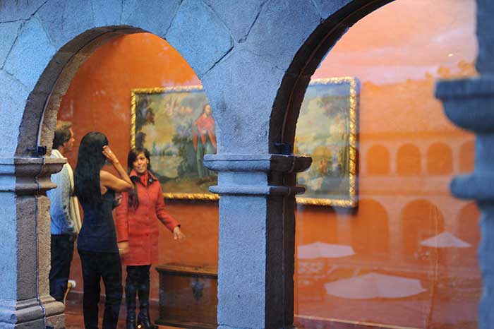 A young guide explaining a couple paintings from the Cusco School in a colonial hotel featuring beautiful arches