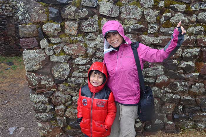 Machu Picchu with Kids, traveler with kid smiling at the camera having Pisaq ruins as backdrop
