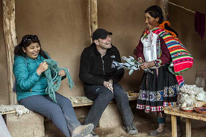 A man and a woman laughing with a local lady of Pampallaqta community within Potato Park, while she explains about natural colors used in her textiles