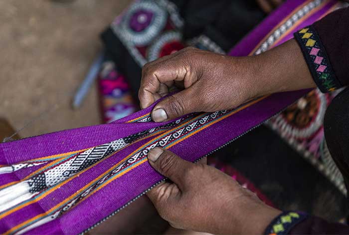 Hands working on a handmade textile with local patterns in Pampallaqta, Potato Park Cusco