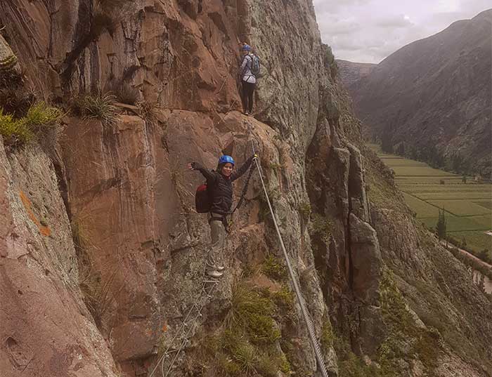 2 travelers and one of them waving from a swinging bridge on their way up to the Skylodge