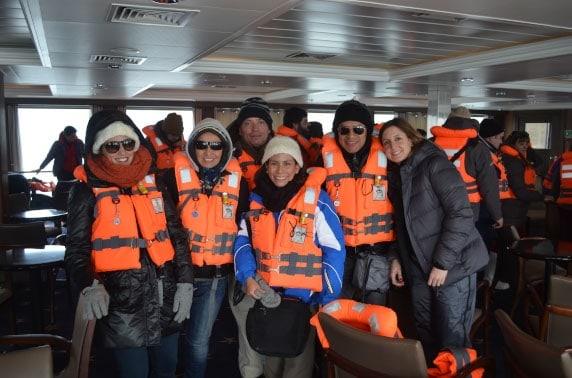 A group of travelers wearing orange life jackets watching at the camera aboard Stella Australis