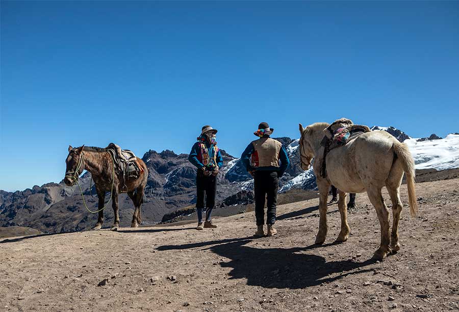 Two horsemen wearing traditional attire with 2 horses waiting for clients at path to the Vinicunca Rainbow Mountain 