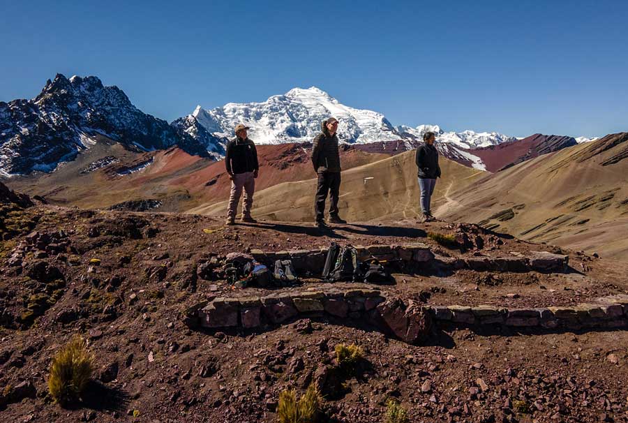 Three travelers on the way to the Red Valley with the Ausangate snowcapped mountains as backdrop