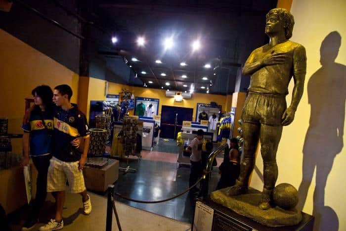 a couple visiting the museum of La Bombonera stadium passing by the Maradona statue.