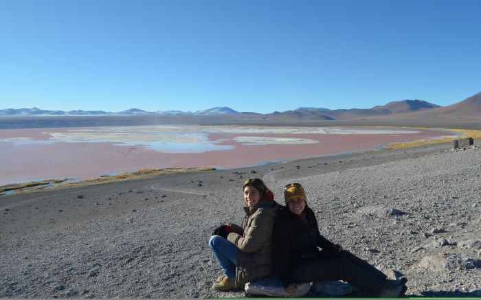Two women posing for a picture with the red lagoon as backdrop in the Eduardo Avaroa Reserve