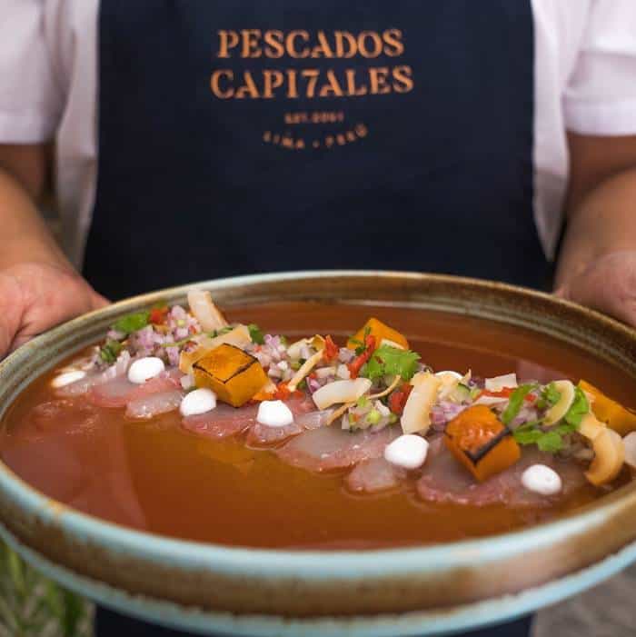 the hands of waiter holding a big plate containing a colorful 'tiradito' (a dish of laminated fish with an orange sauce)