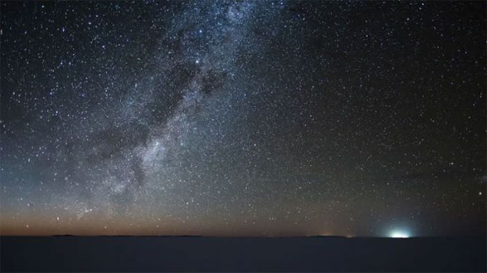 a starry sky and a light in the distance in the salt flats of Uyuni