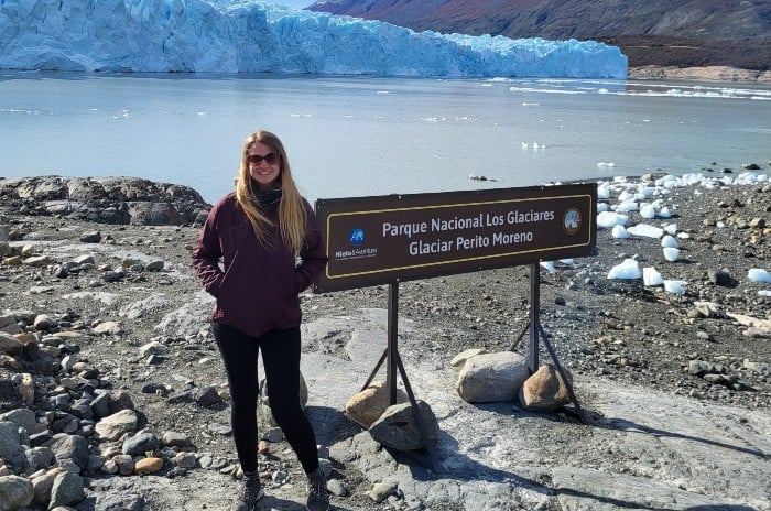 Female traveler wearing sun glasses and smiling with Perito Moreno glacier as backdrop