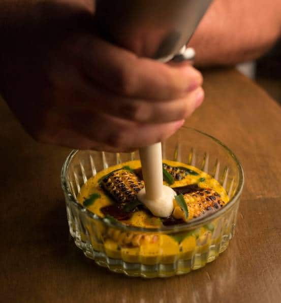 two hands using a pastry bag to put a white sauce as topping on a circulate plate  with a yellow cream