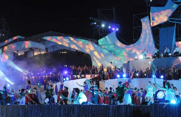 Dozens of people wearing color attires on an illuminated stage by night dancing and celebrating the Harvest Festival in Mendoza Argentina