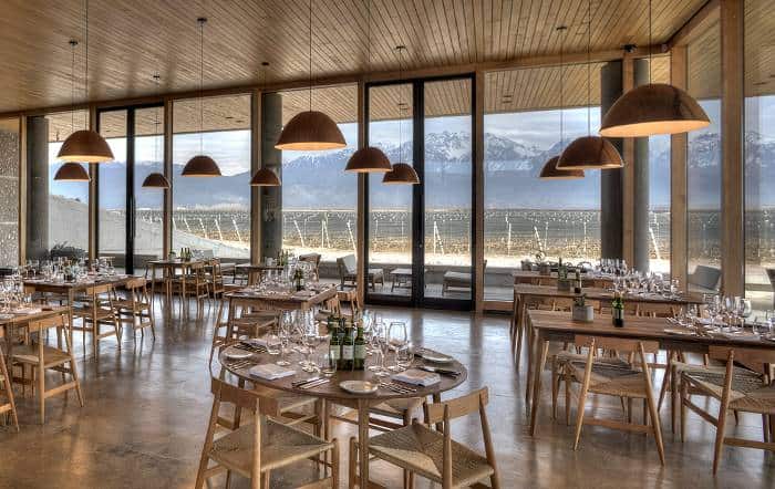 an empty resraurant with modern wooden furniture overlooking a vineyard and snowcapped mountains at Zuccardi wine state