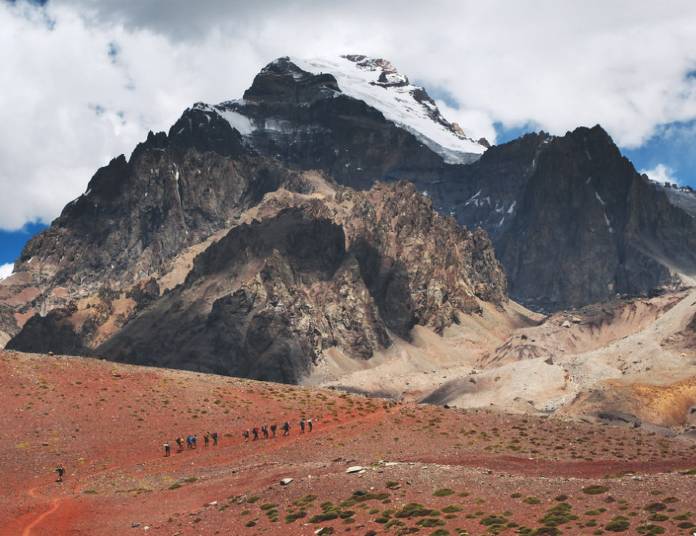 Walkers in a line along a trail with a snow-capped mountain on the horizon