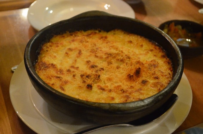 Spider crab chowder in black bowl served on white plate with a spoon