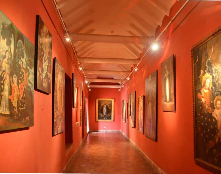 Colonial room with walls painted in red displaying colonial paintings at the MAP Museum in Cusco