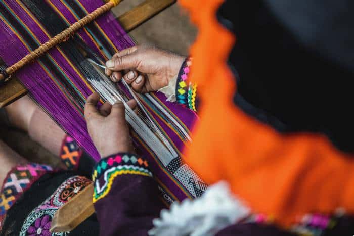 Hands of a female artisan wearing a traditional attire weaving with wool threads