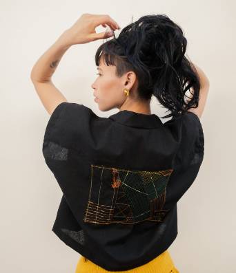 A model with tied black hair wearing a handmade black blouse with an embroidery in the back  
