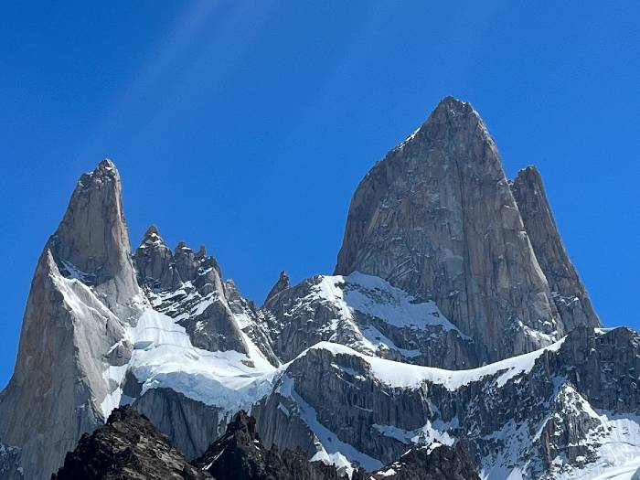 The Fitz Roy mount of granite partially covered by snow with a blue sky in the background. This mount is the highlight of El Chalten hiking region in Argentina