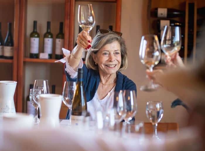 A blond lady toasting with a glass of white wine.